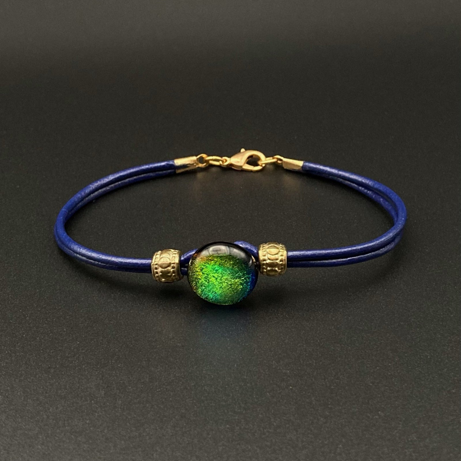 Blue leather bracelet with a round green glass focal and gold accent beads, by 3D Glass Designs.