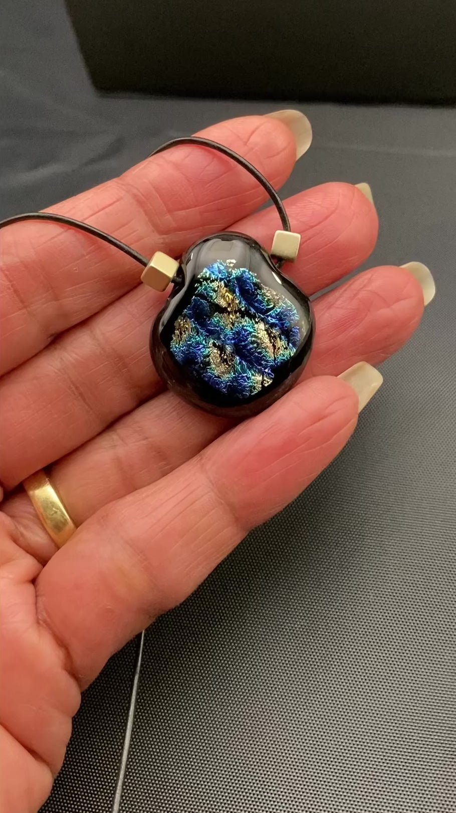 Hand holding fused glass pendant against a black cloth background, by 3D Glass Designs.