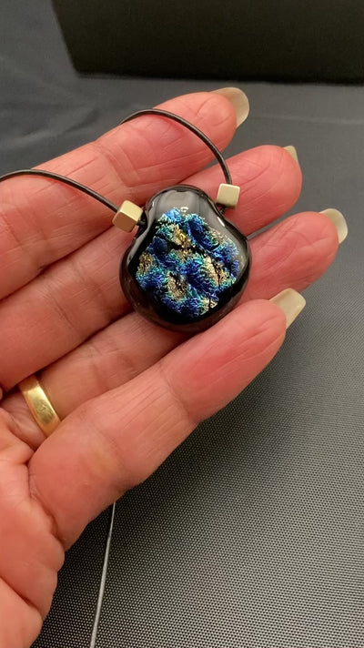 Hand holding fused glass pendant against a black cloth background, by 3D Glass Designs.