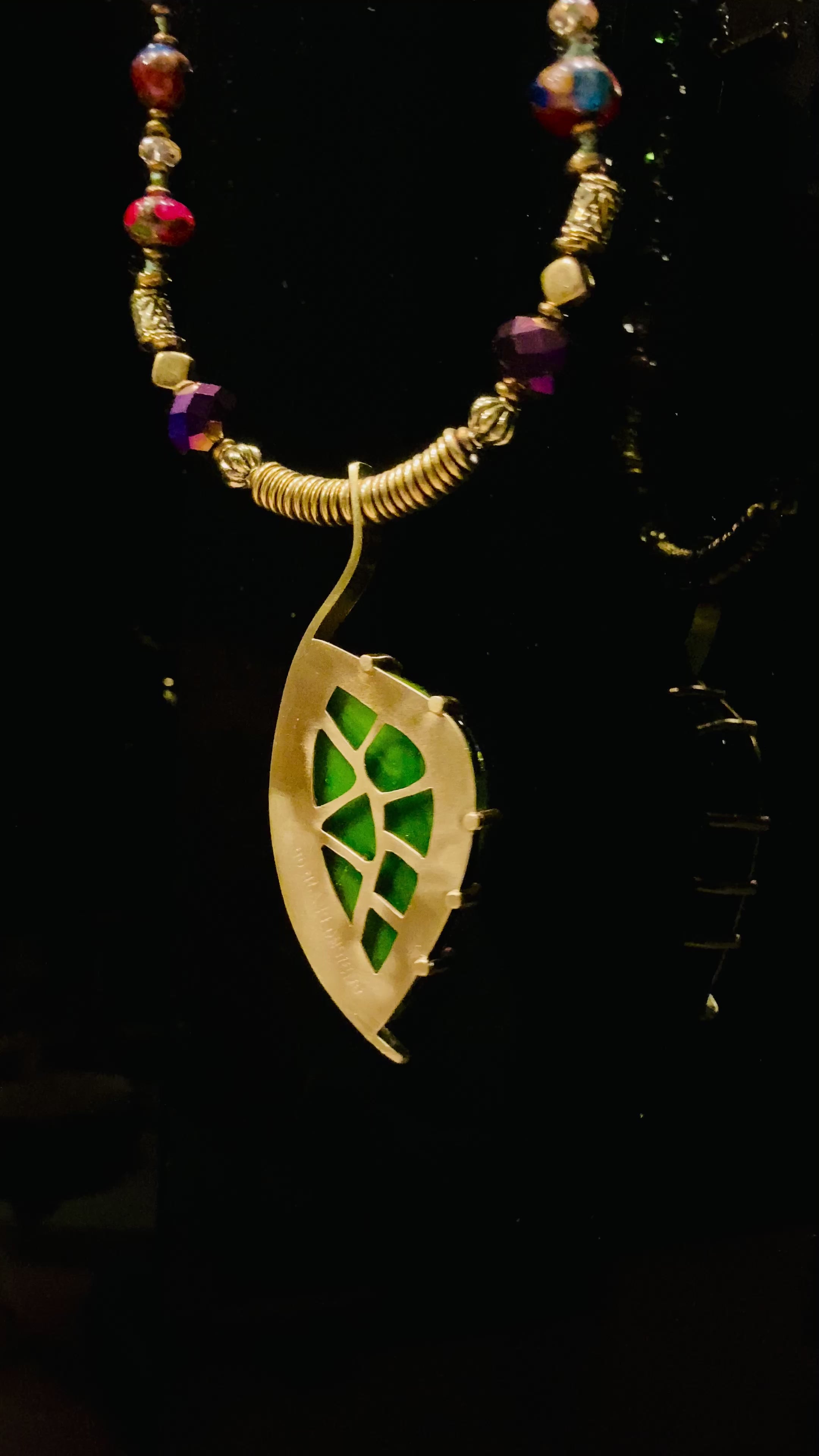 Video of dichroic glass set in a unique brass pendant, with prongs on left side and a textured bezel on the right side. Pendant is hung on a 29" long hand-knotted multicolor beaded necklace, by 3D Glass Designs. of 
