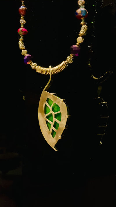 Video of dichroic glass set in a unique brass pendant, with prongs on left side and a textured bezel on the right side. Pendant is hung on a 29" long hand-knotted multicolor beaded necklace, by 3D Glass Designs. of 