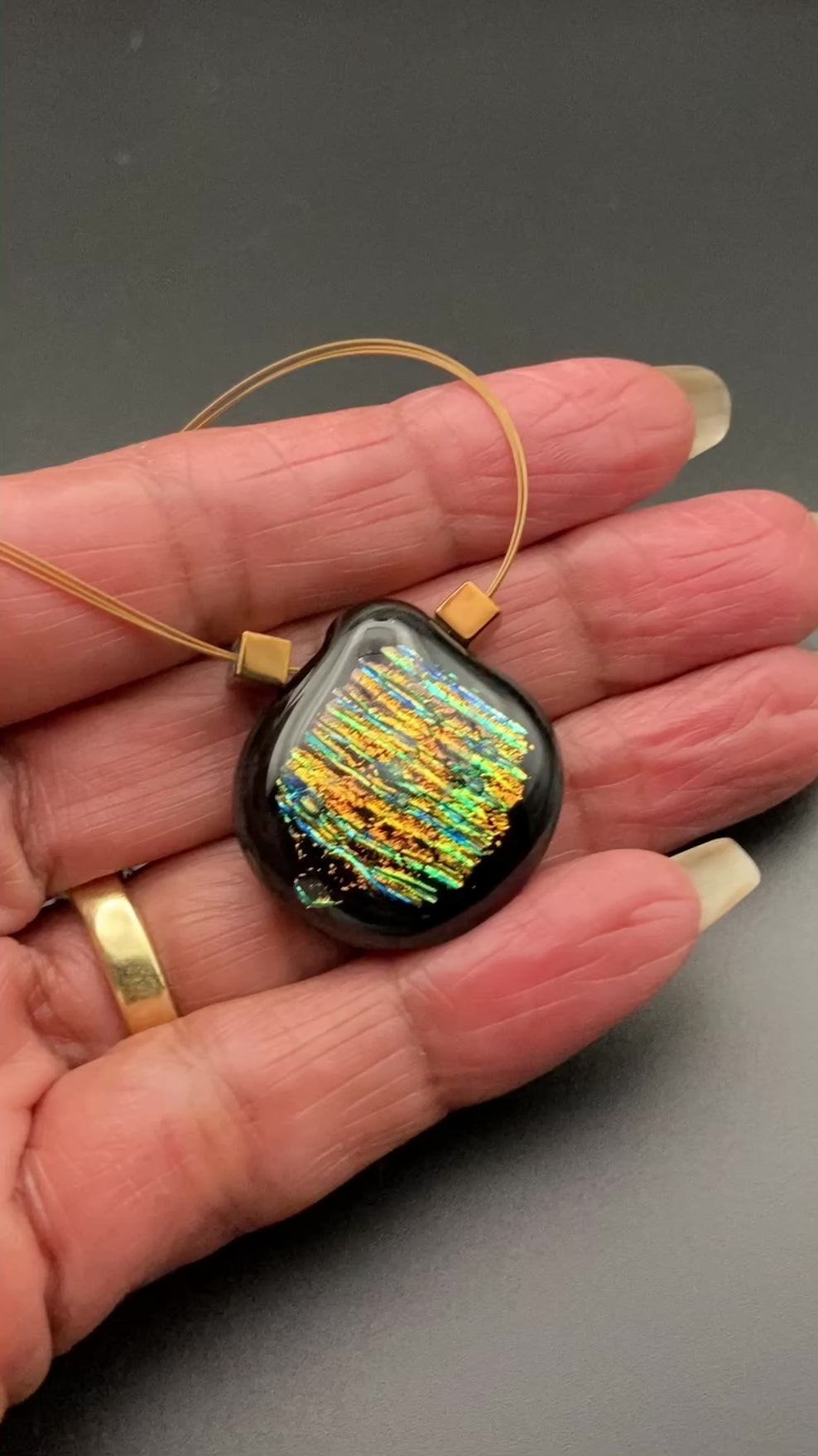 Hand holding dichroic glass pendant, by 3D Glass Designs.