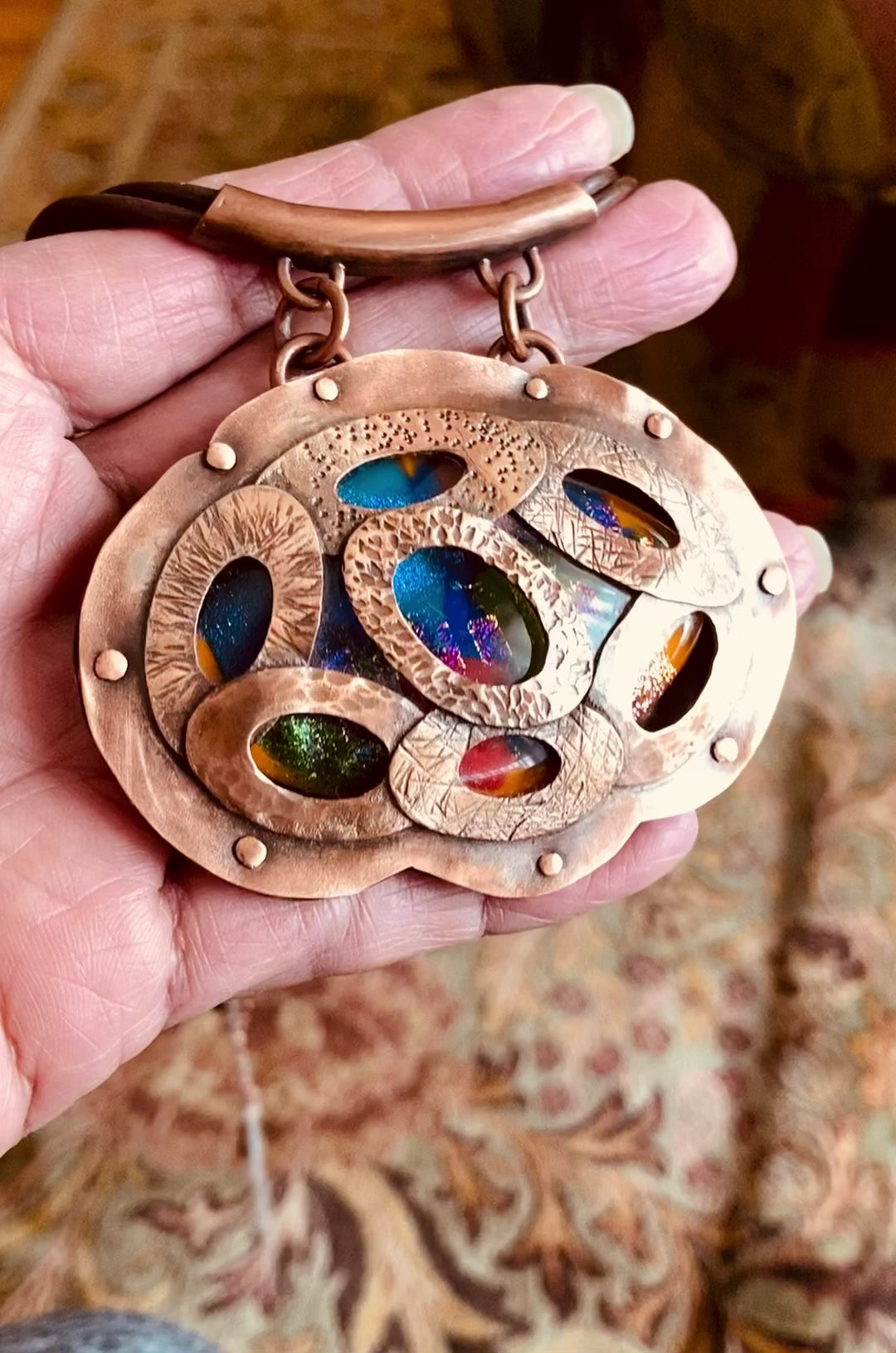 Video of Artisan designed copper and fused glass pendant, oval shaped with overlapping copper ovals on top, revealing colorful glass beneath. By 3D Glass Designs