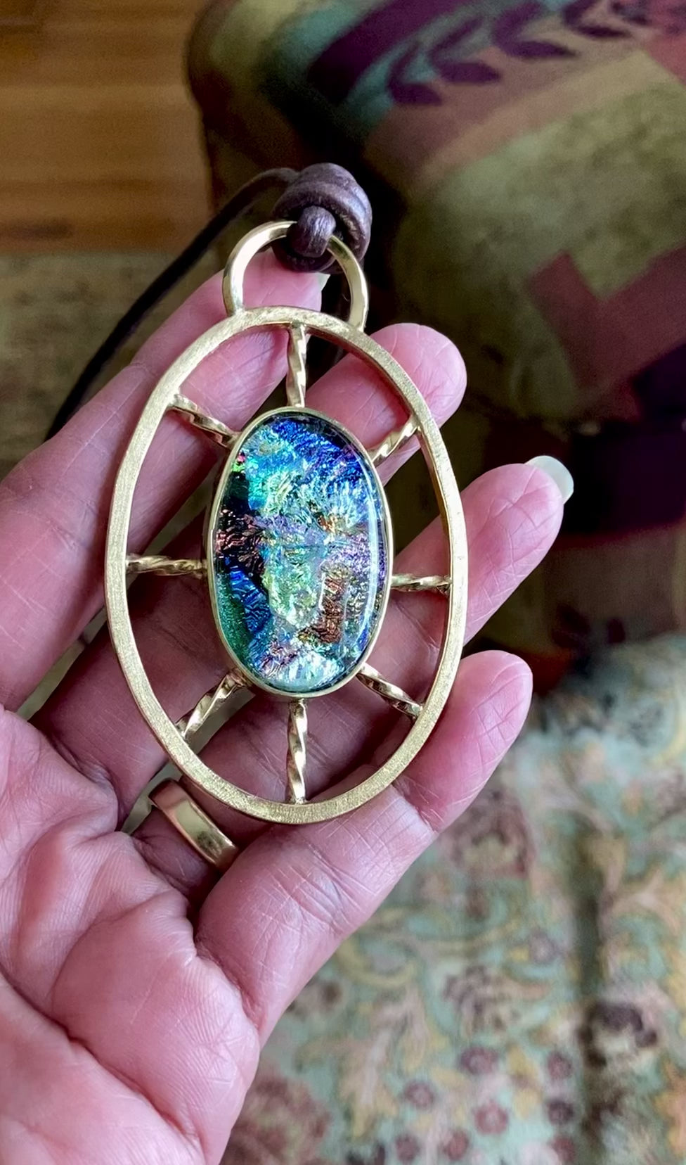 Video of hand holding Dichroic glass set in a unique brass pendant, with prongs on left side and a textured bezel on the right side. Pendant is hung on a 29" long hand-knotted multicolor beaded necklace, by 3D Glass Designs.
