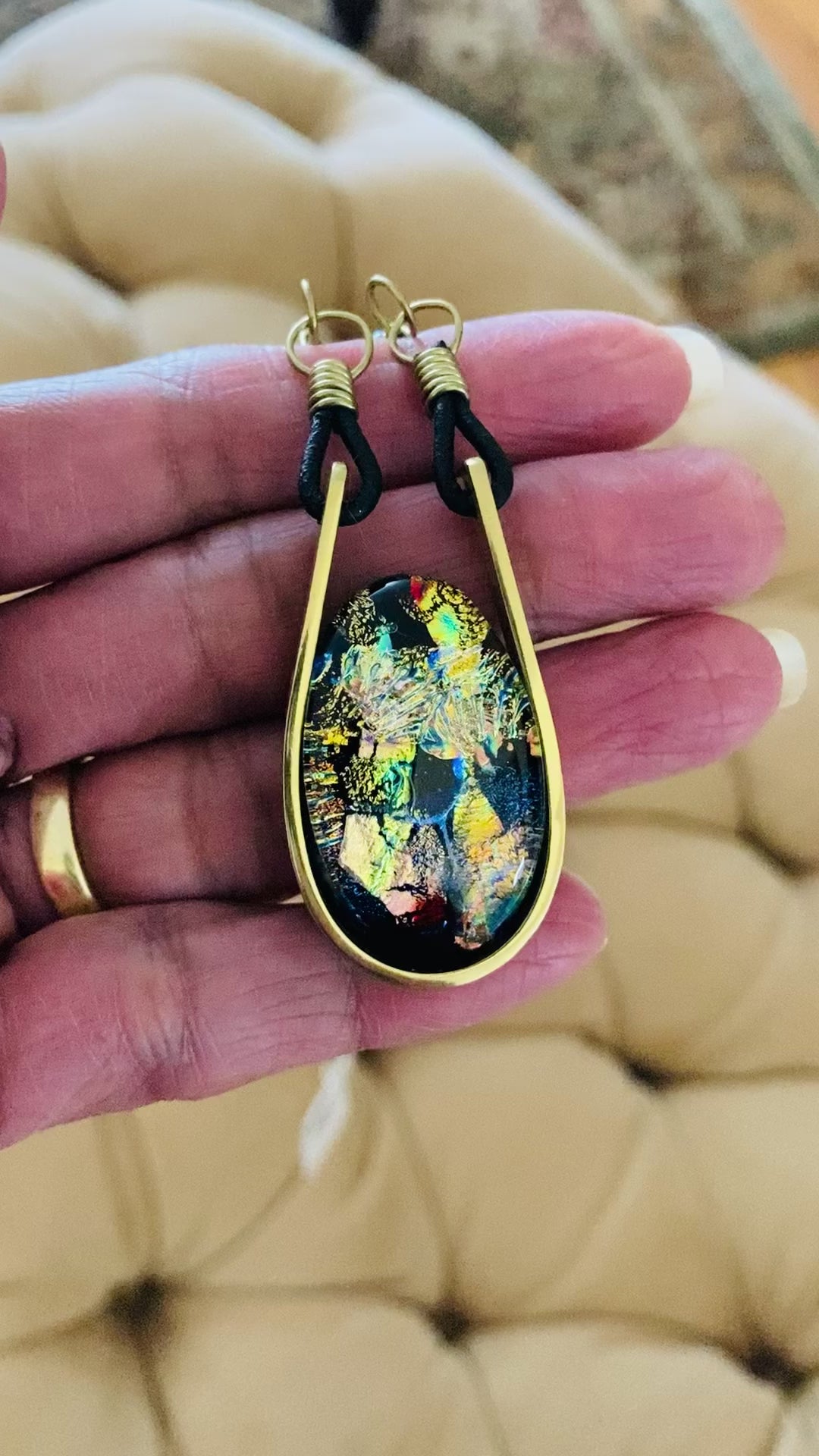 Models hand holding modern fused dichroic glass and brass pendant with a beaded leather cord, by 3D Glass Designs.