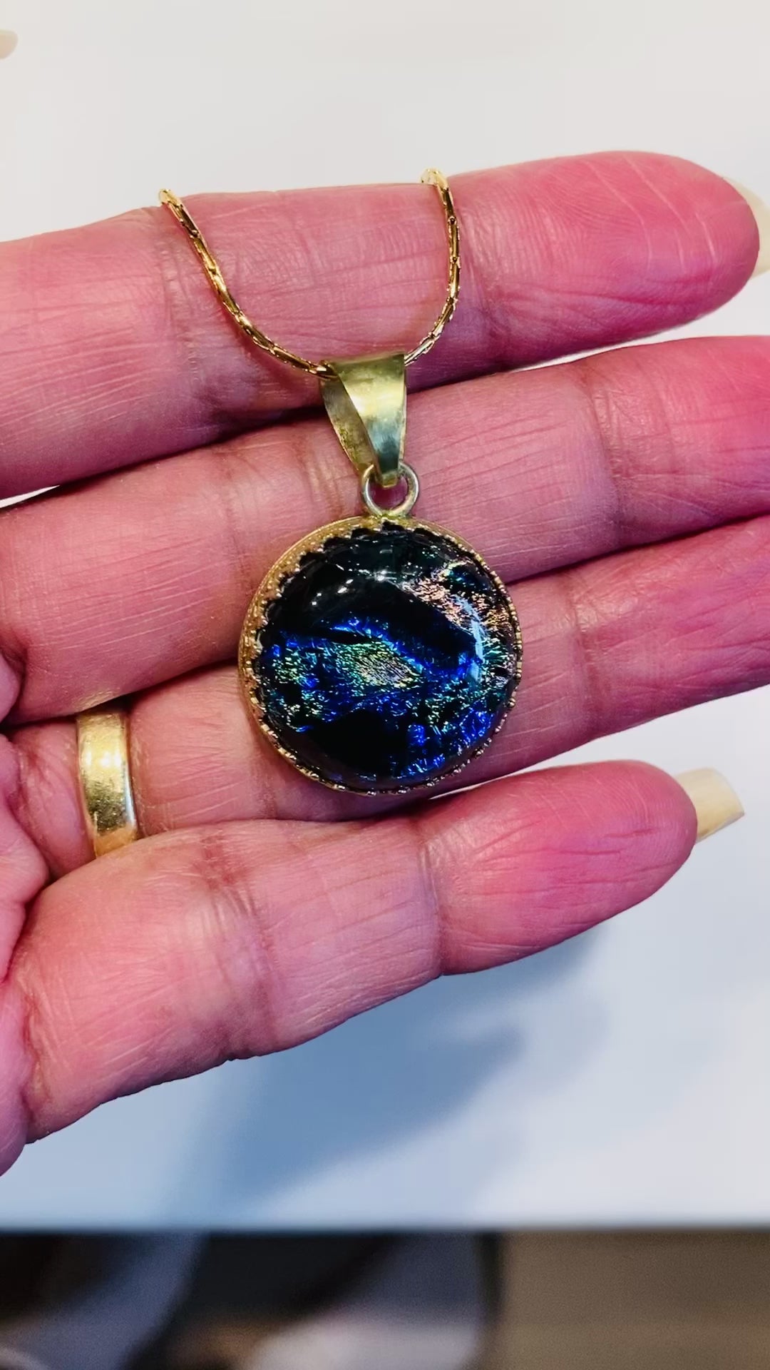 Video of hand holding a small dichroic glass pendant by 3D Glass Designs.