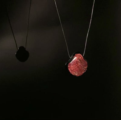 Dichroic glass pendant rotating against a shiny black background with its reflection on the left, by 3D Glass Designs.