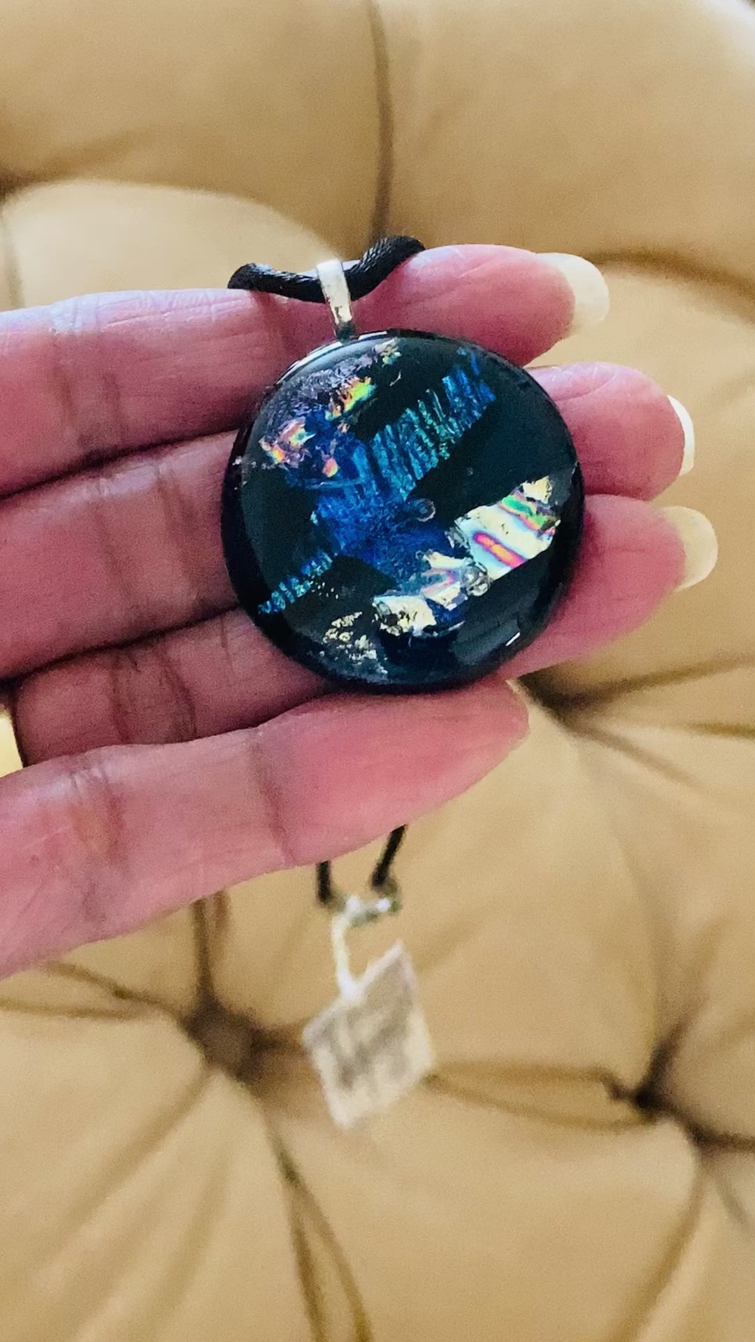 Hand holding round dichroic glass pendant, by 3D Glass Designs.