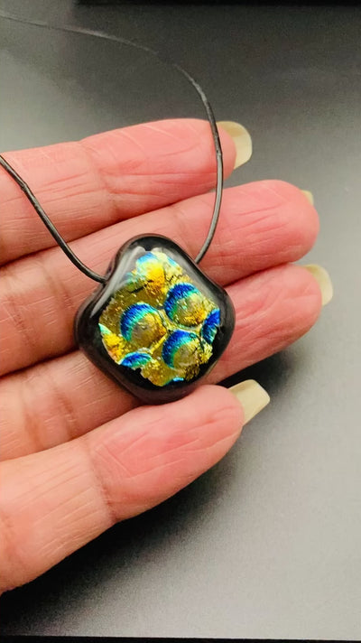 Hand holding a small, fused glass pendant, by 3D Glass Designs.