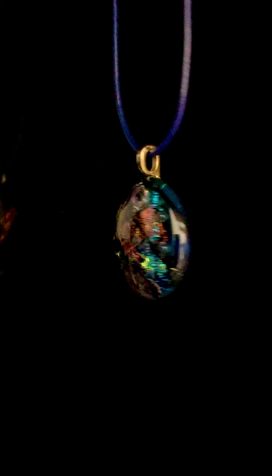 Video of fused glass pendant on a blue leather cord. Transparent blue glass with layers of red, rust, blue, green and purple dichroic glass and a copper squiggle design embedded in the glass. By 3D Glass Designs