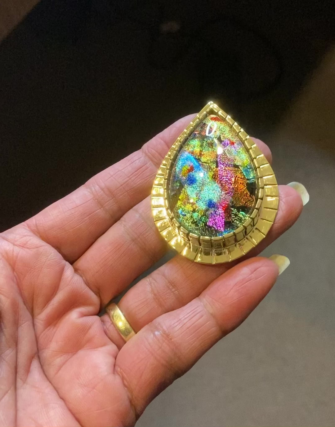 Video of colorful teardrop shaped dichroic pendant set in a custom brass setting. By 3D Glass Designs.