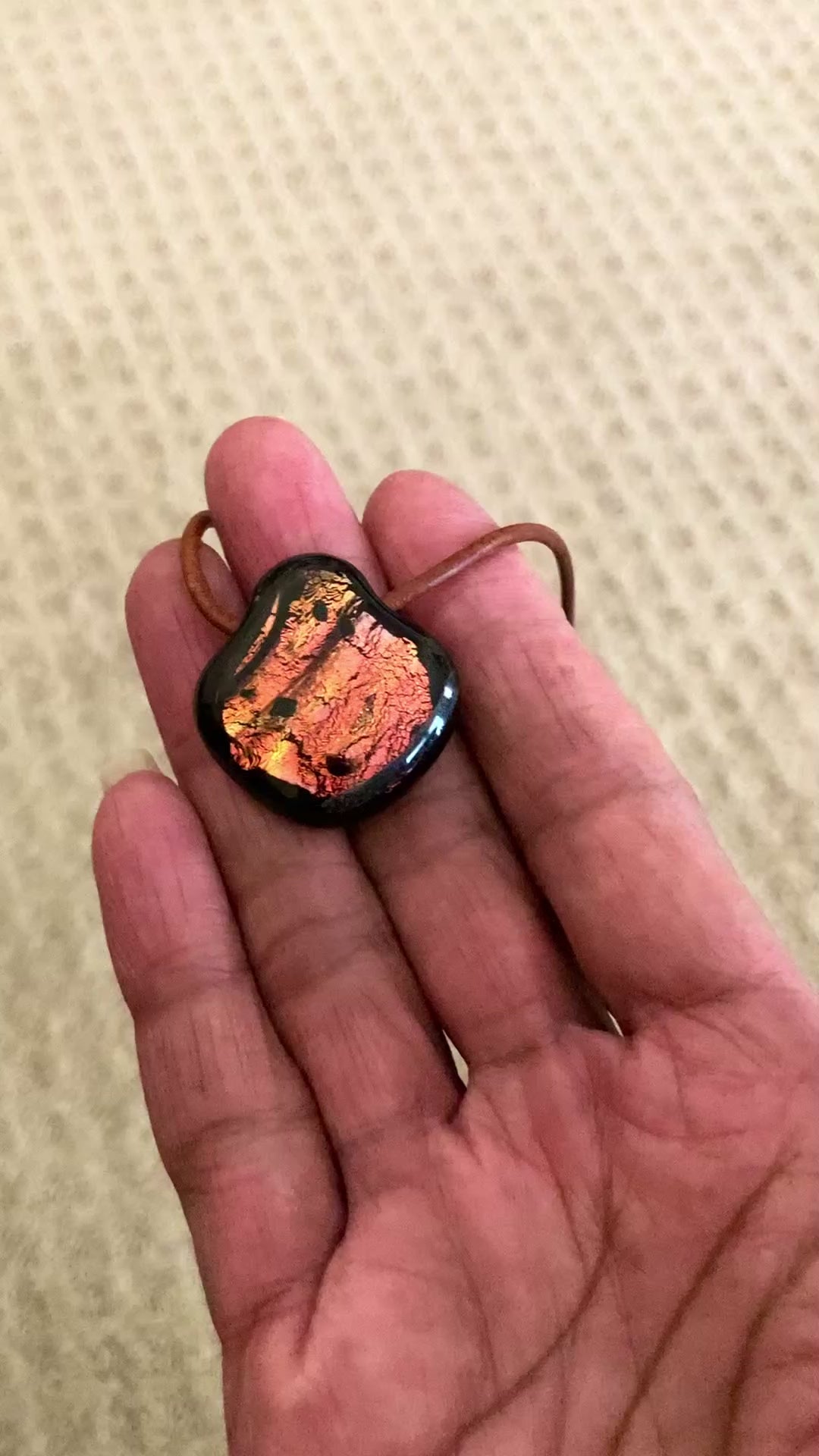 Models hand holding a fused glass pendant against a beige background, by 3D Glass Designs.