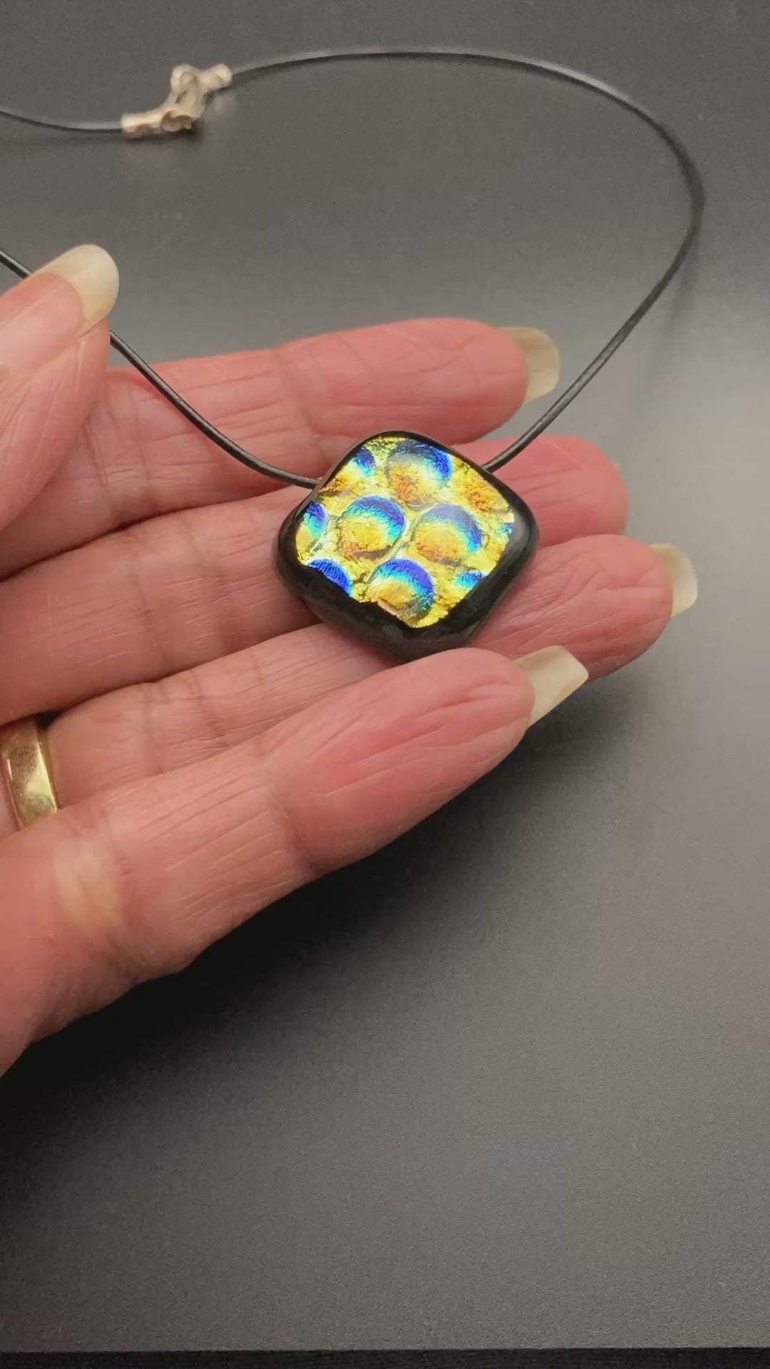 Hand holding fused glass pendant against a black background, by 3D Glass Designs.