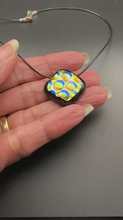 Hand holding fused glass pendant against a black background, by 3D Glass Designs.