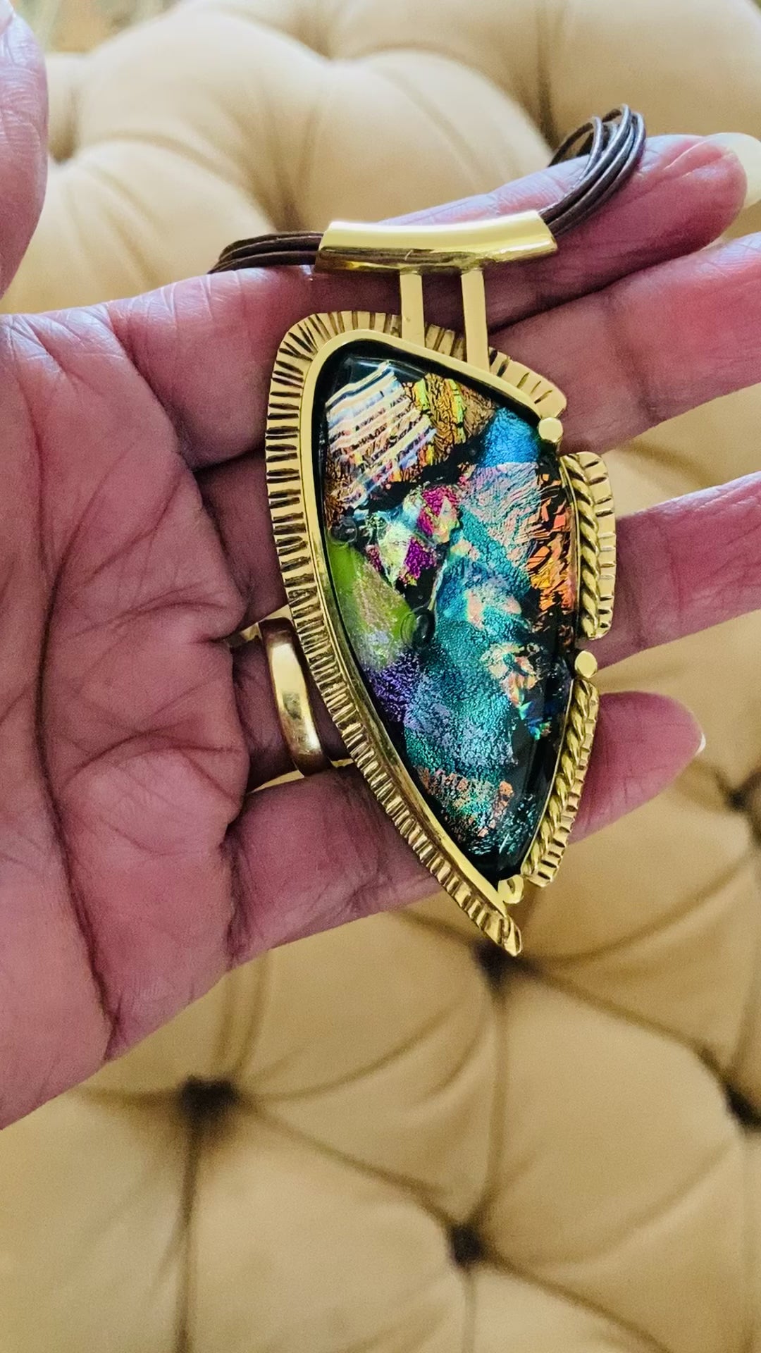 Video of hand holding handcrafted multicolor fused glass set in brass on a multistrand leather necklace, by 3D Glass Designs.