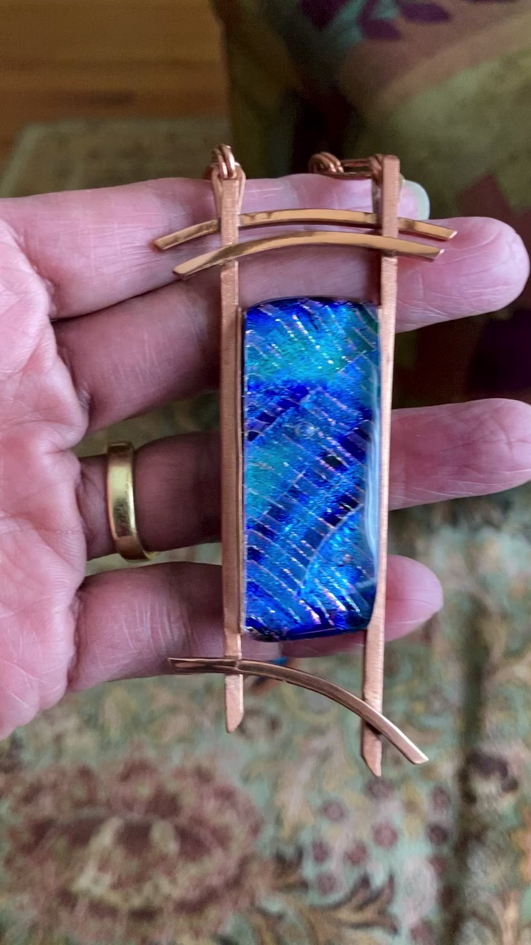 Video of hand holding blue dichroic glass set in handcrafted copper pendant with an Asian design. Handmade copper paperclip link chain completes the design, by 3D Glass Designs
