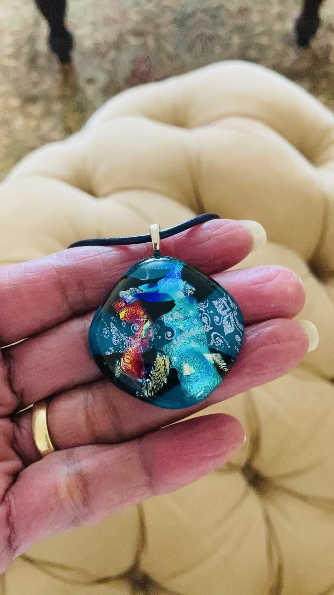 Video of model holding dichroic glass pendant in teal, red, silver, blue and gold, by 3D Glass Designs.